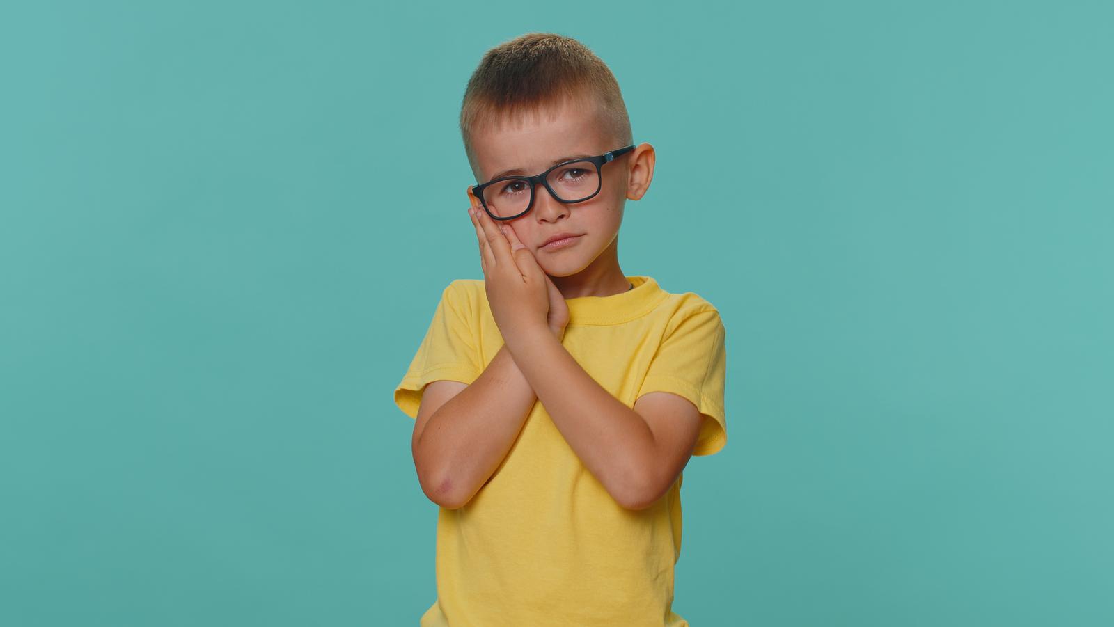 A young boy wearing glasses and covering his face with his hands while receiving tips for keeping his teeth healthy.